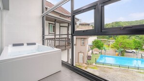 A modern bathroom with a large bathtub and a view of a swimming pool and greenery outside. - Gapyeong Shiny Pension (Gapyeong)