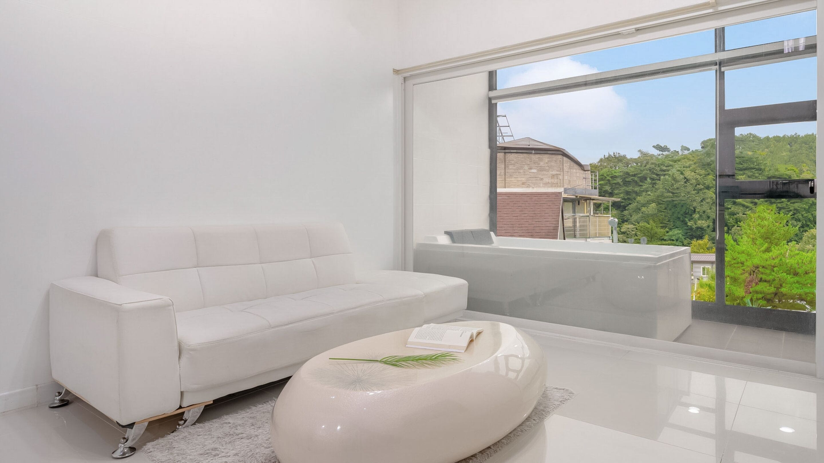 A modern living room with a white sofa, a glossy coffee table, and a large window offering a view of a building and greenery.