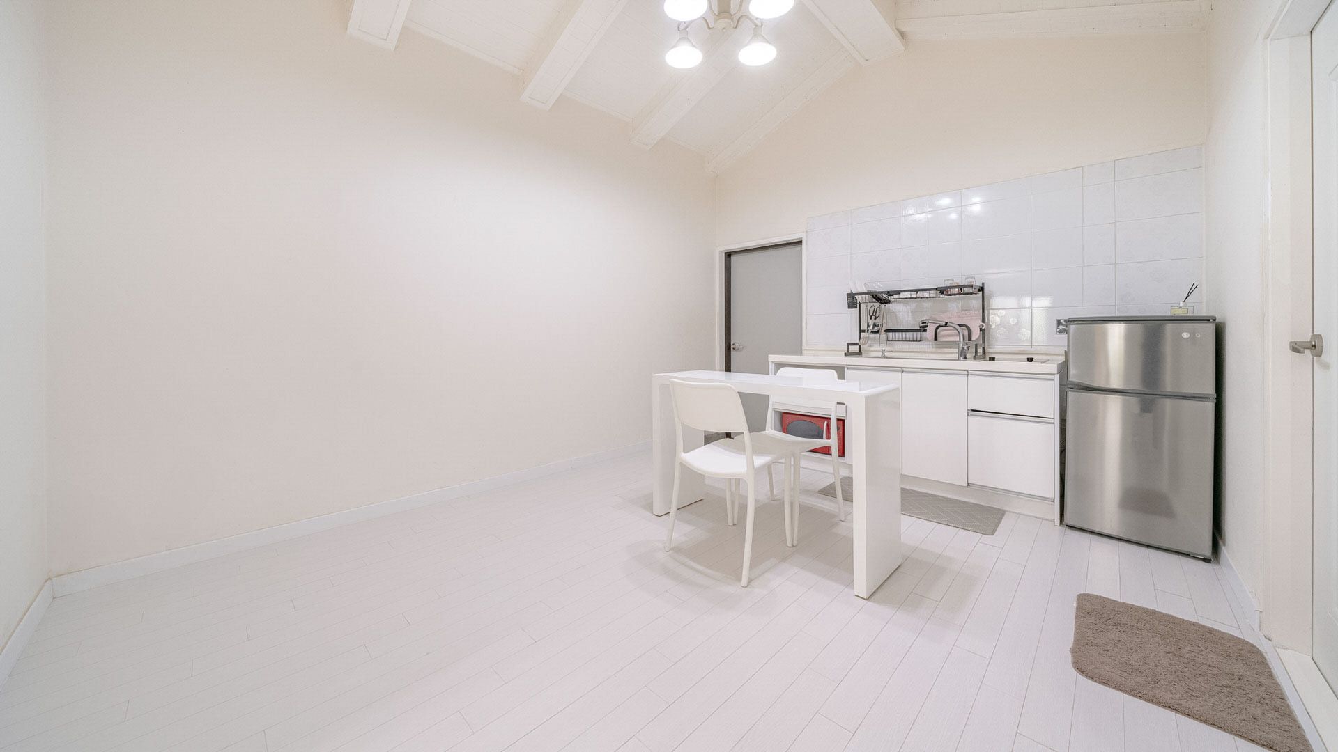 Una cocina moderna con armarios blancos, un refrigerador de acero inoxidable y una zona de comedor con una mesa y una silla blancas.