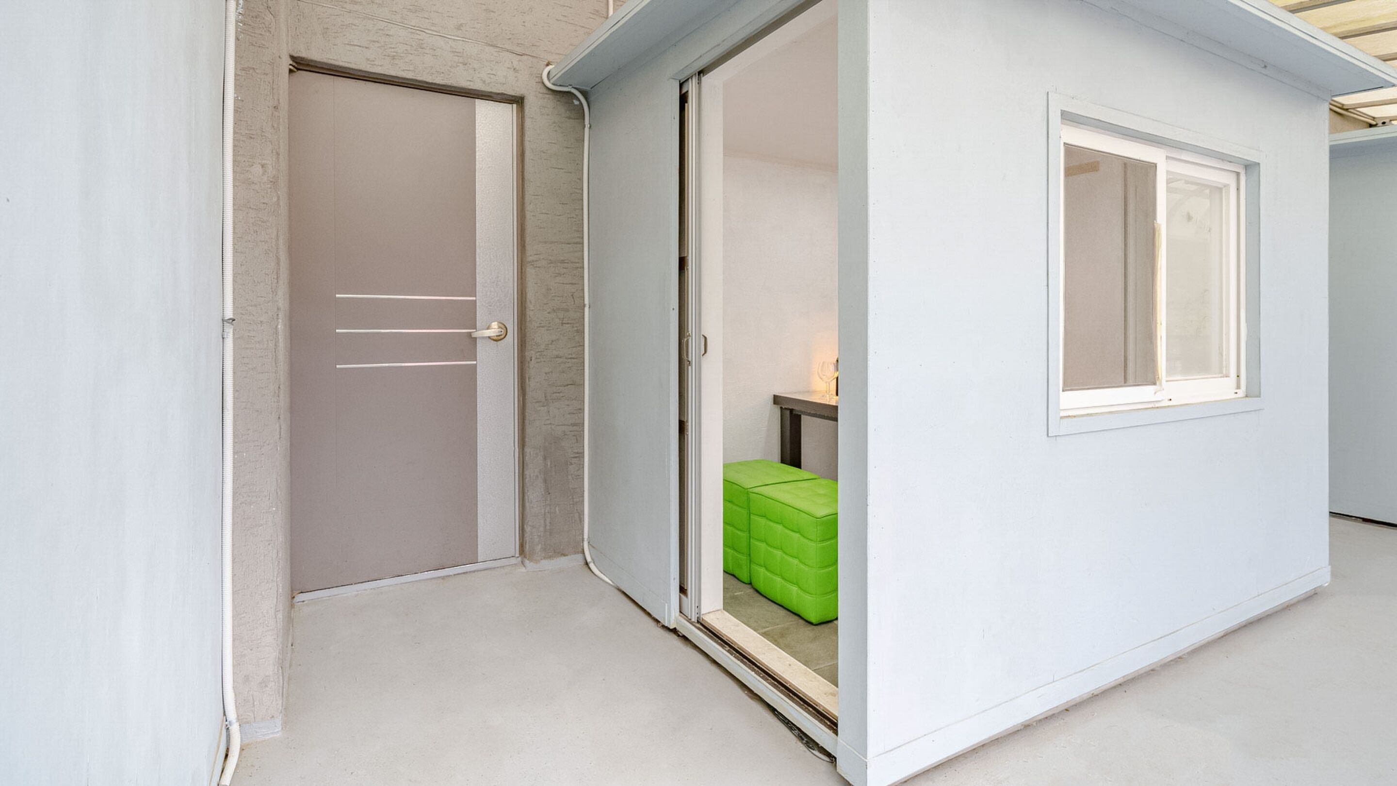 A small, enclosed room with a sliding door, a window, and a green storage box.