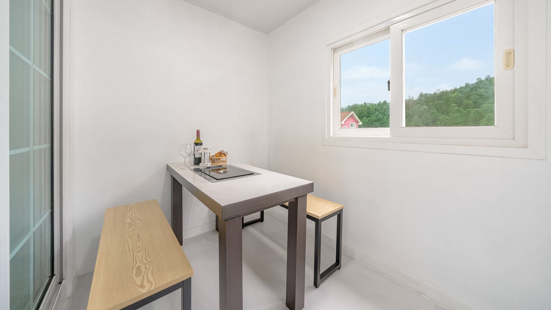 A small, clean room with a table, bench, and a window with a view of greenery.