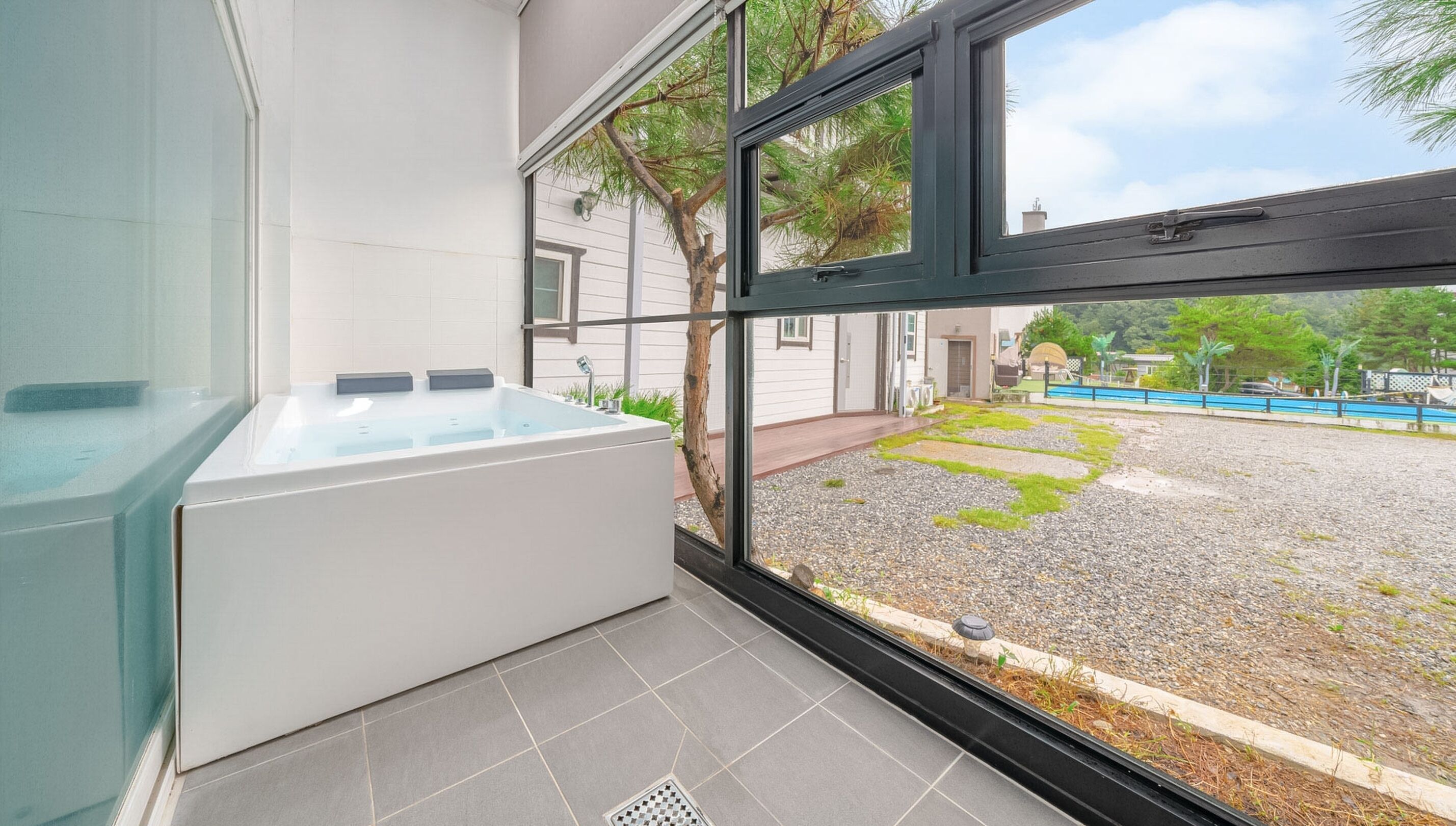A modern bathroom with a large bathtub, a window with a view of a garden and a pool.