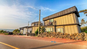 A modern two-story house with a stone wall and a balcony. - Jeju Kkothyanggi Badasori Pension (Jeju City)