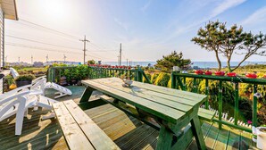 A wooden deck with a picnic table, surrounded by a green railing and potted plants. - Jeju Kkothyanggi Badasori Pension (Jeju City)