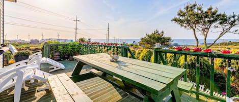 A wooden deck with a picnic table, surrounded by a green railing and potted plants.