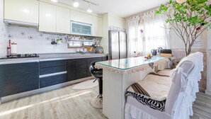 A modern kitchen with a central island, dark cabinetry, and a view of a dining area with a white chair. - Jeju Kkothyanggi Badasori Pension (Jeju City)