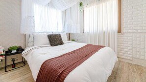 A neatly made bed with white bedding and a red throw blanket, a small bedside table with a plant, and sheer curtains. - Jeju Kkothyanggi Badasori Pension (Jeju City)