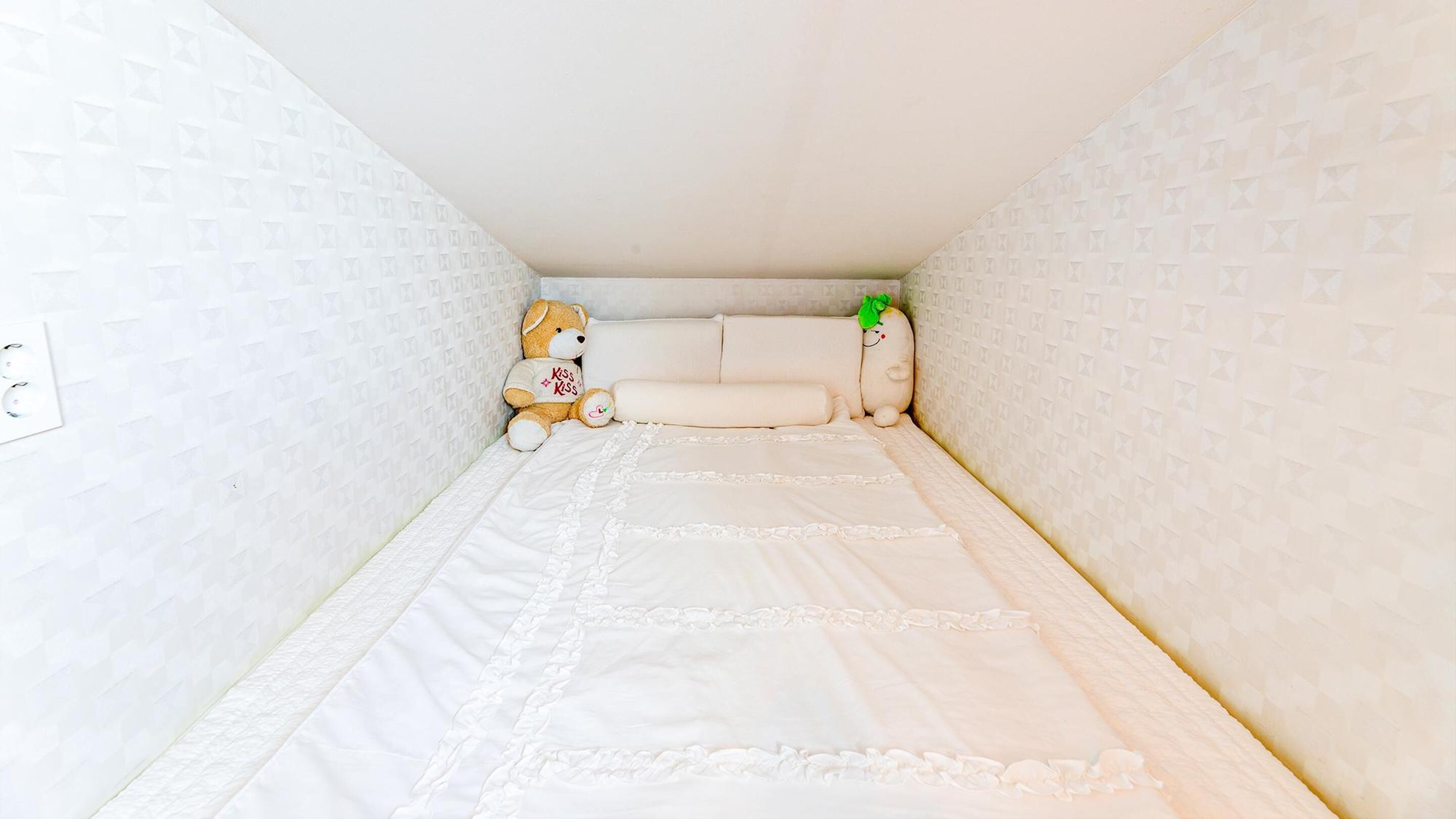 Um quarto pequeno e estreito com uma cama de solteiro, um urso de pelúcia e uma pequena planta.