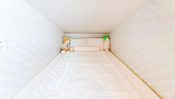 Um quarto pequeno e estreito com uma cama de solteiro, um urso de pelúcia e uma pequena planta.