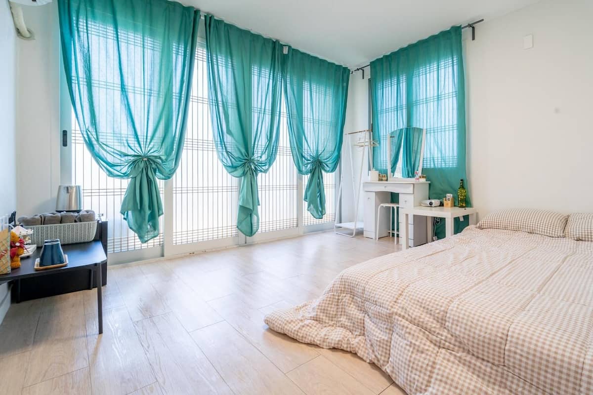 Une chambre avec un grand lit, un bureau avec une chaise, un miroir et une fenêtre avec des rideaux.