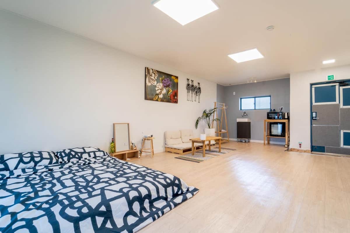 Une pièce spacieuse avec un grand lit, un bureau, une chaise, une petite table, une plante et un tableau au mur.