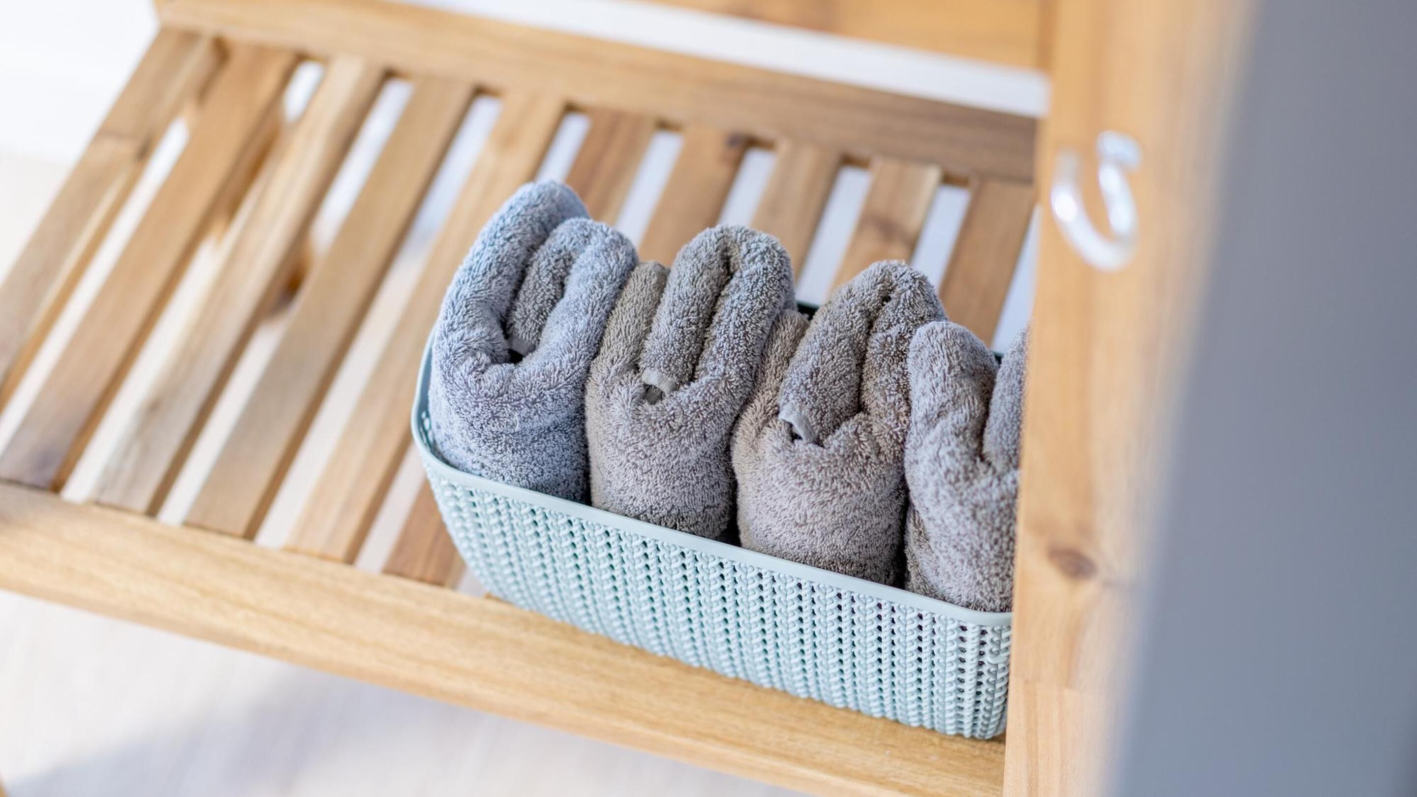 A wooden bench with a woven basket containing several gray towels.