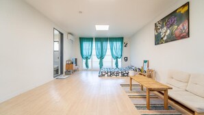 A spacious living room with a sofa, a coffee table, and a bed with patterned bedding. - Jeju Dalbam Pension (Seogwipo)