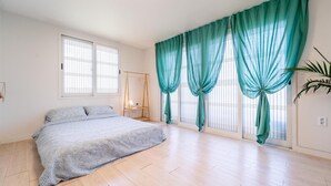A bedroom with a bed, a wooden floor, a window with blinds, and a plant. - Jeju Dalbam Pension (Seogwipo)