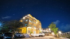 A multi-story hotel with balconies, a parking area, and a starry night sky. - Jeju Dalbam Pension (Seogwipo)