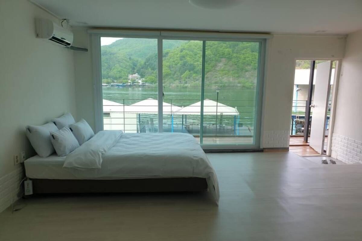 Un dormitorio con un amplio ventanal corredera que da a un balcón con vistas a un lago y edificios.