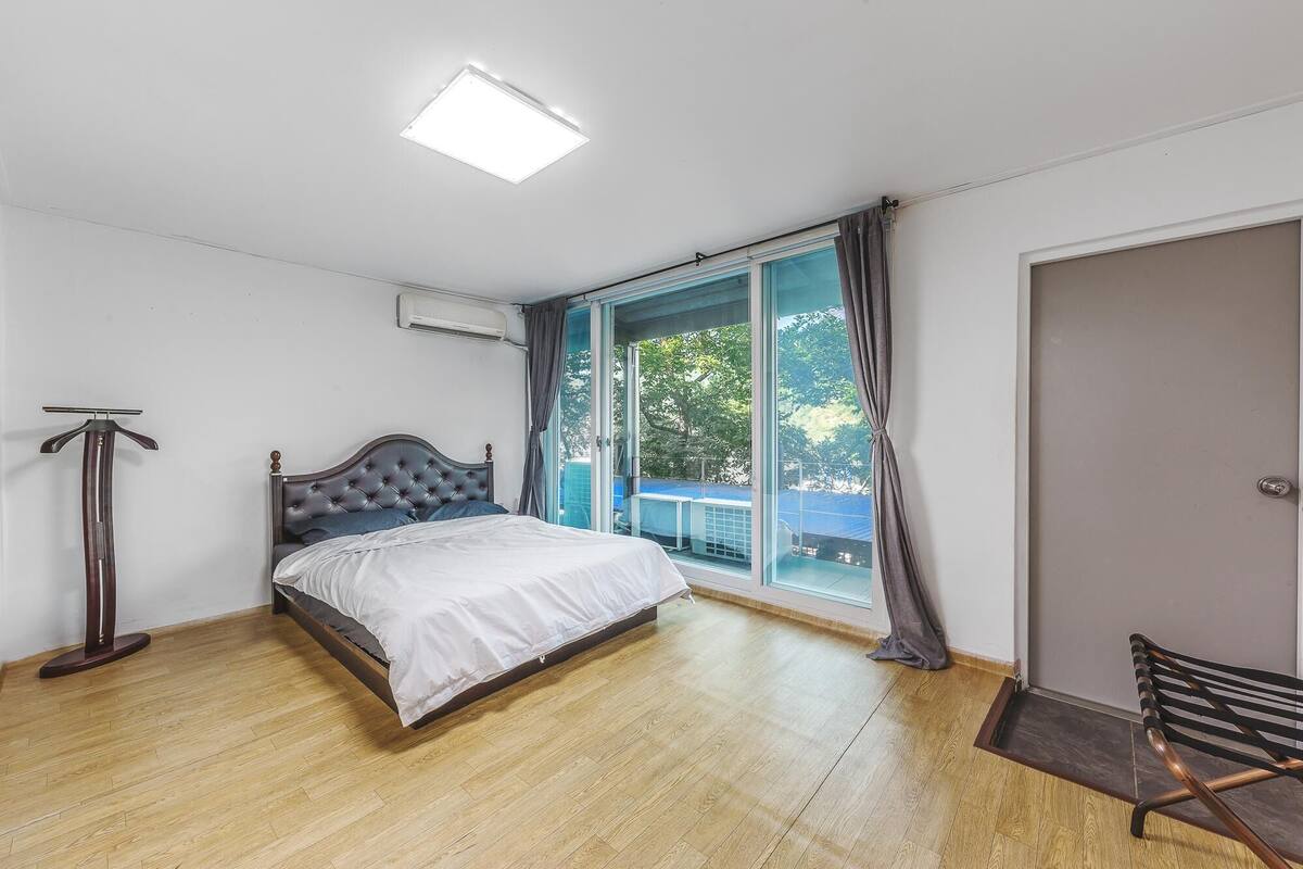 Un dormitorio con cama, lámpara de pie, ventana con cortinas y una puerta.