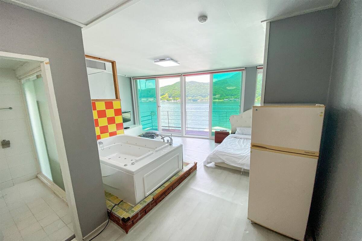 Una habitación con bañera, cama y refrigerador.