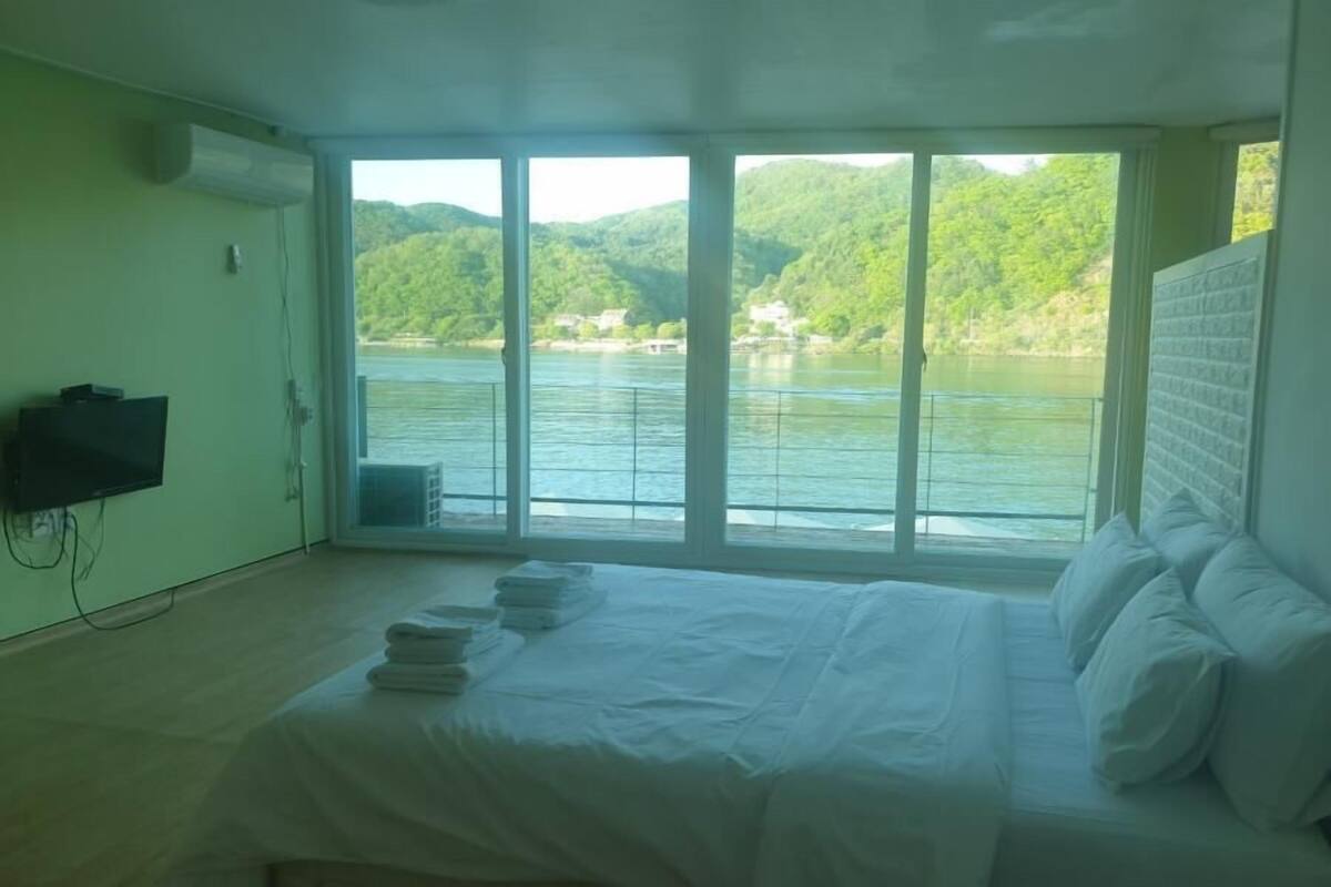 Un dormitorio con un ventanal grande que da a un lago y colinas.