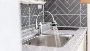 Un lavamanos de cocina con agua corriente, un grifo moderno y un salpicadero de azulejos grises.
