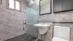 Un baño moderno con cabina de ducha de vidrio, lavabo blanco y retrete.