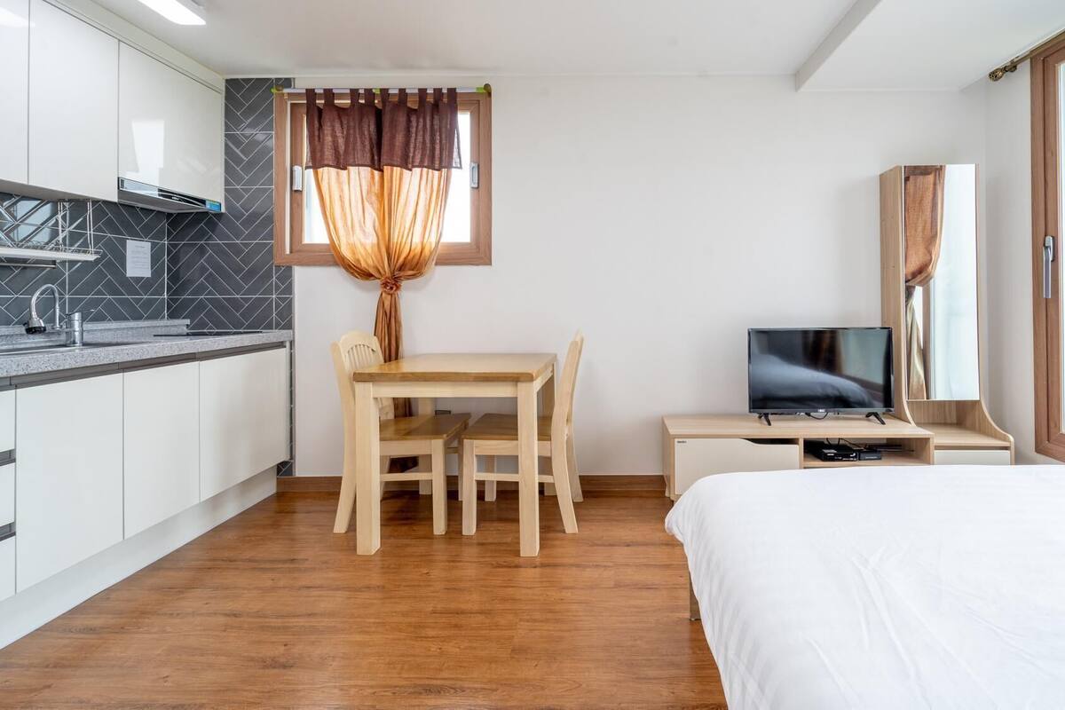A modern hotel room with a wooden dining table, a TV, and a bed.