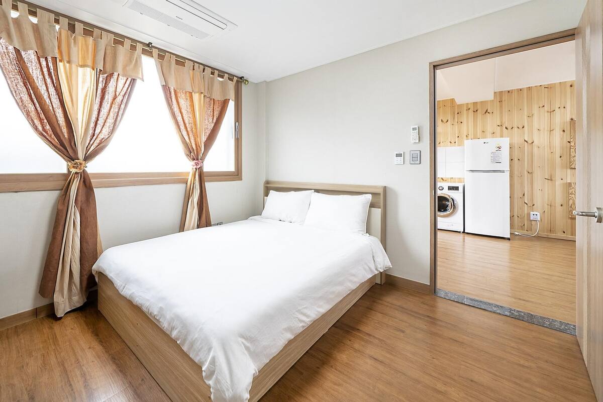 A bedroom with a wooden bed, white bedding, and a window with curtains.