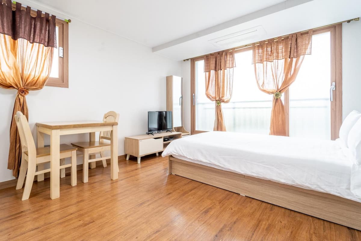 A hotel room with a wooden desk, a television, a bed, and curtains.