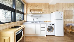 A modern kitchen with wooden cabinetry, a built-in oven, a washing machine, and a refrigerator.