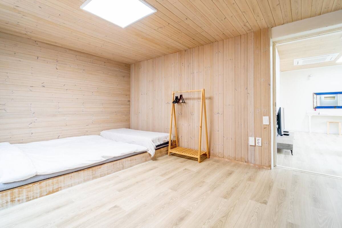 A minimalist room with a bed, a wooden wardrobe, and a bathroom visible through an open door.