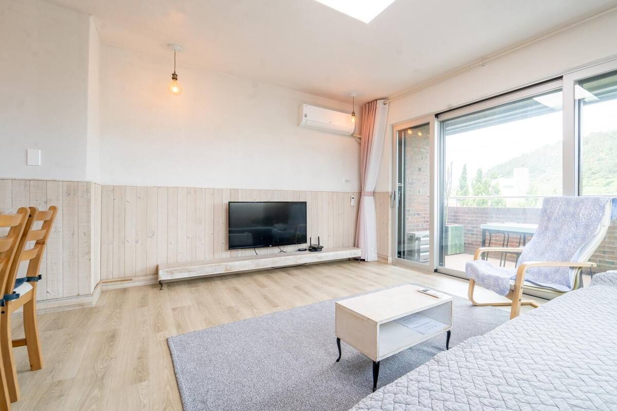 A modern living room with a flat-screen TV, wooden panel walls, a large sliding glass door, and a cozy seating area.