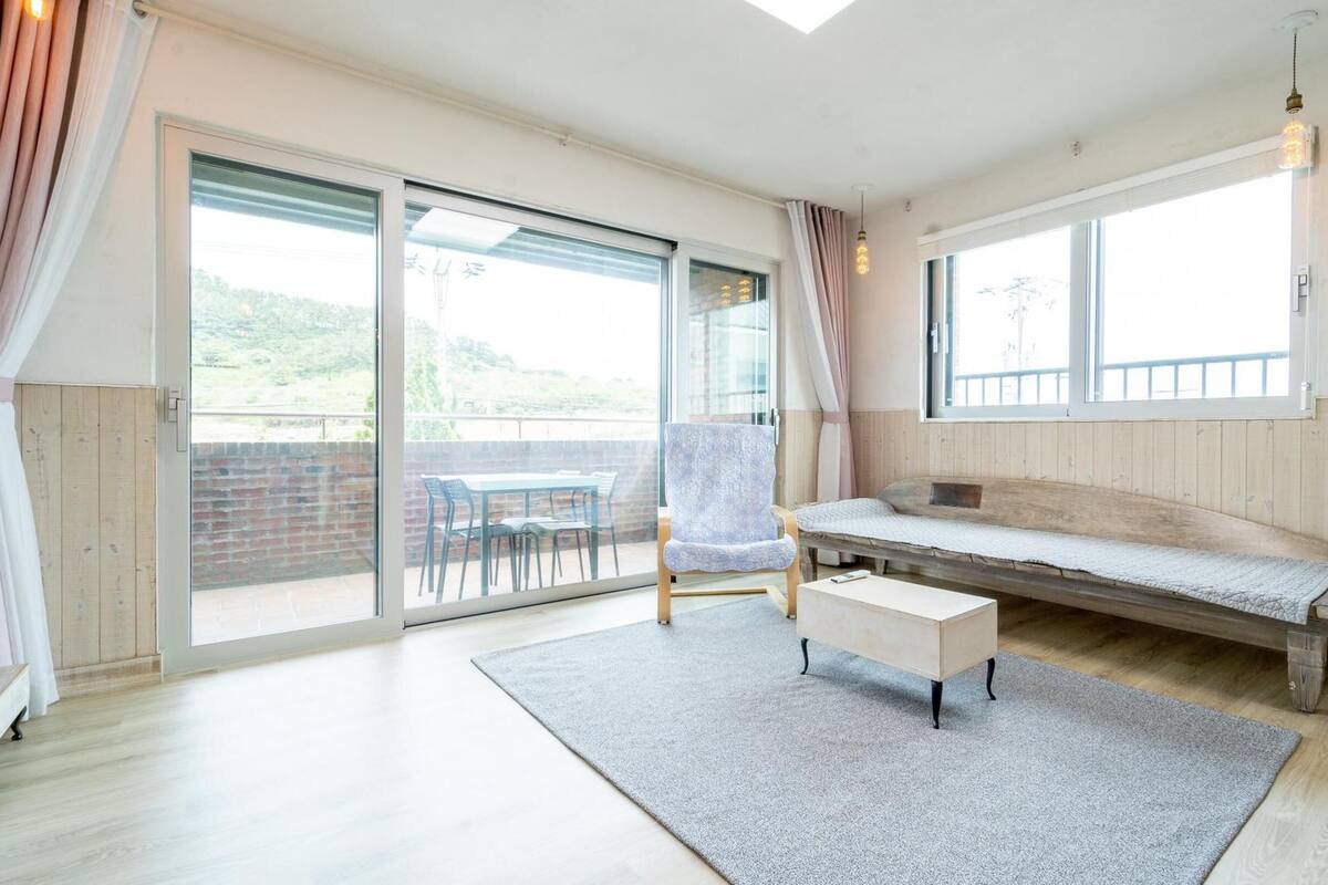 A spacious room with a large sliding glass door leading to an outdoor area, a wooden bench, a chair, and a small table.