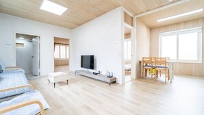 Une pièce spacieuse avec un plancher en bois, un lit, une télévision, un bureau et un coin repas avec des chaises.