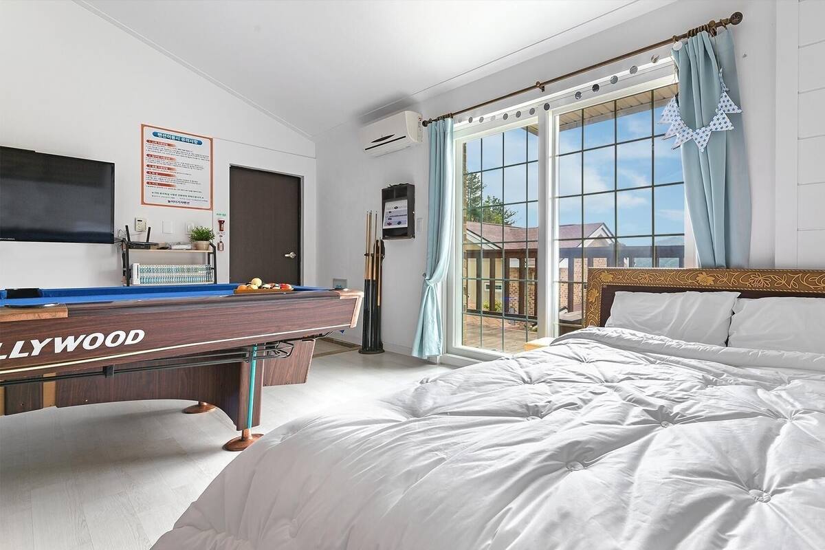 A bedroom with a pool table, a bed, and a large window.