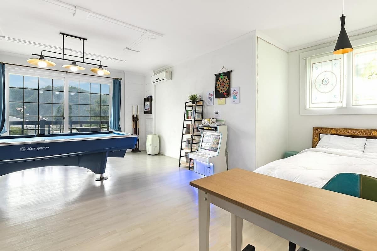 A room with a pool table, a bed, a desk, and a window with a view.