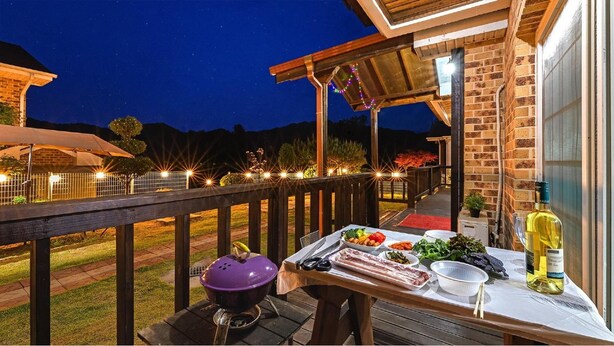 An outdoor dining area with a barbecue grill, a table set with food, and a bottle of wine. - Gapyeong Peulrei38 Pension (Gapyeong)