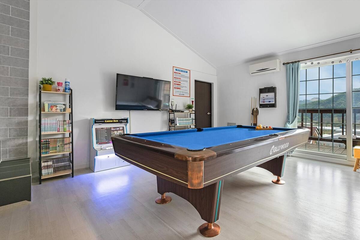 A modern hotel room with a pool table, a Game Box, a TV, and a balcony with a view.