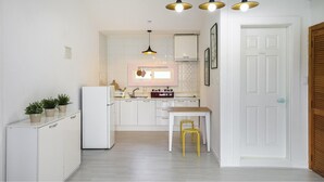 A compact kitchen with white cabinets, a white refrigerator, a wooden dining table with a yellow stool, and pendant lighting. - Gapyeong Peulrei38 Pension (Gapyeong)