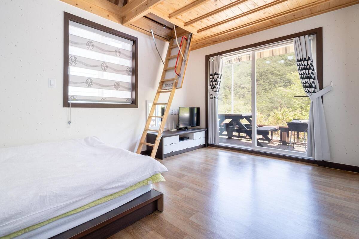 Un dormitorio con cama, televisor, escalera y puerta corrediza a un balcón.