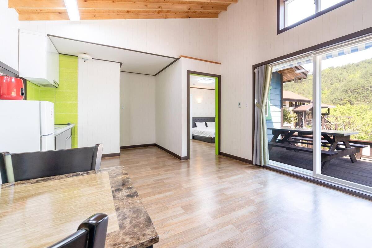Amplia habitación con piso de madera, una mesa de comedor y un amplio ventanal corredero que da a una terraza exterior con una mesa de picnic.
