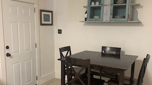 A dining area with a white door, a framed picture, a teal cabinet with dishes, and a tiled floor. - Canal Run Condo on Intracoastal Waterway (Gulf Shores)
