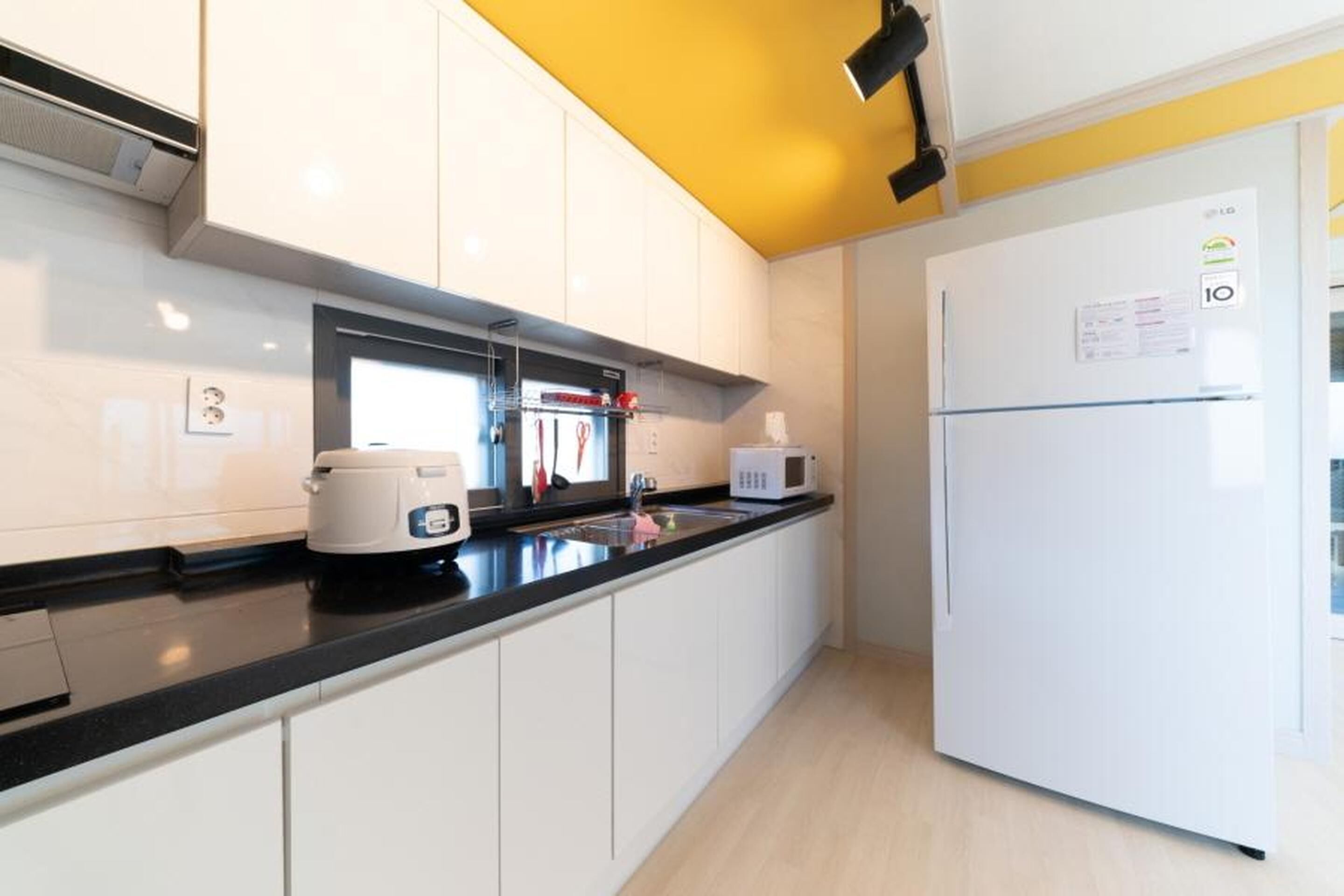 Una cocina moderna con armarios blancos, encimera negra, microondas, tostadora y refrigerador.