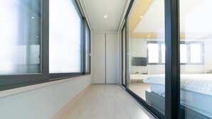 A modern hotel room with a large sliding glass door leading to a balcony, a bed with white bedding, and a bedside table. - Busan Haeoream Pension (Busan)