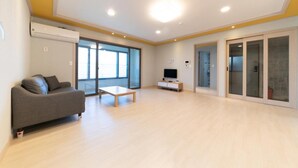 A spacious living room with a sofa, a coffee table, and a television. - Busan Haeoream Pension (Busan)