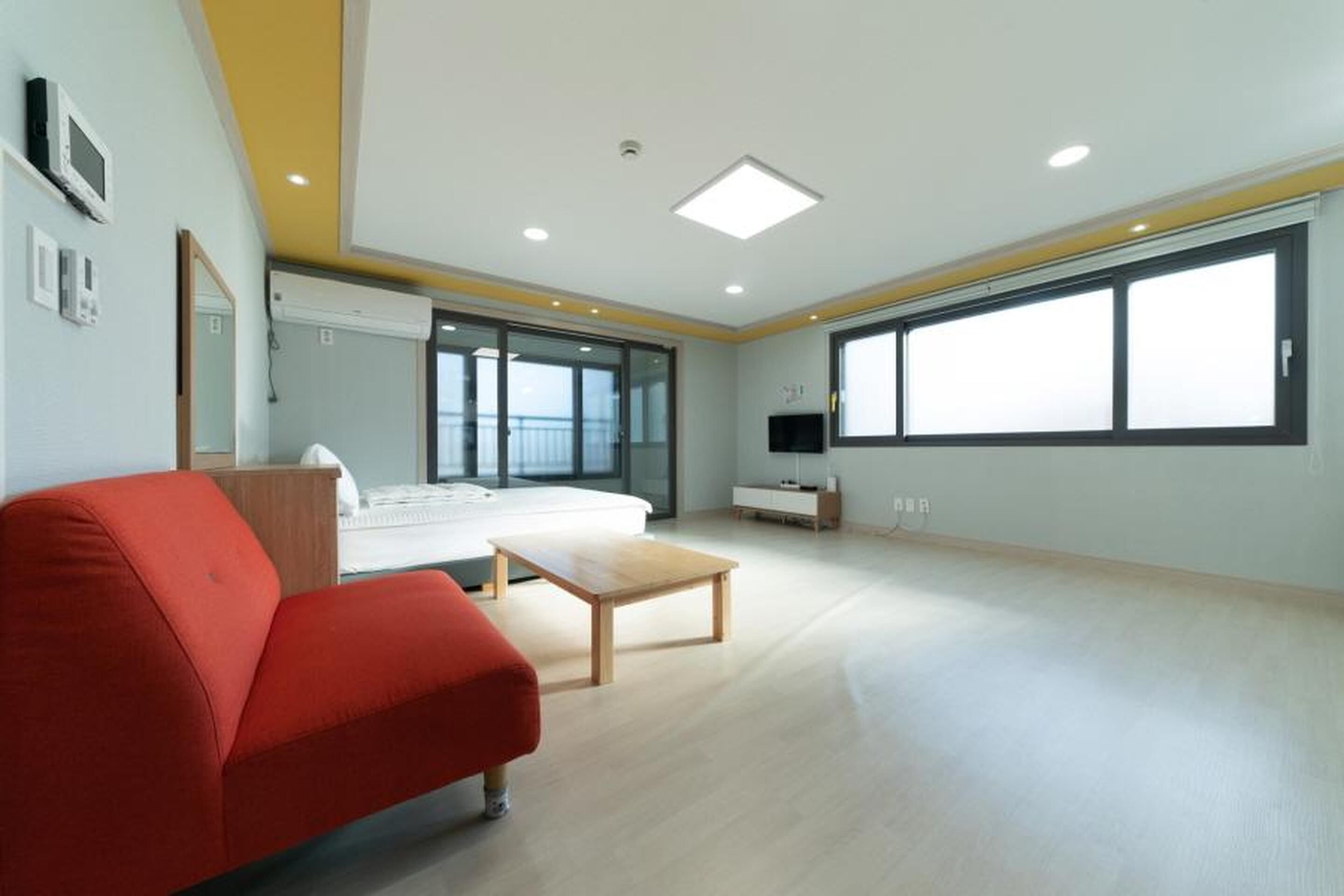 A modern hotel room with a large bed, a red sofa, a wooden coffee table, and a TV.