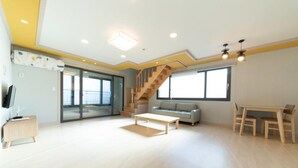 A spacious living room with a wooden staircase, a sofa, a coffee table, and a dining area. - Busan Haeoream Pension (Busan)