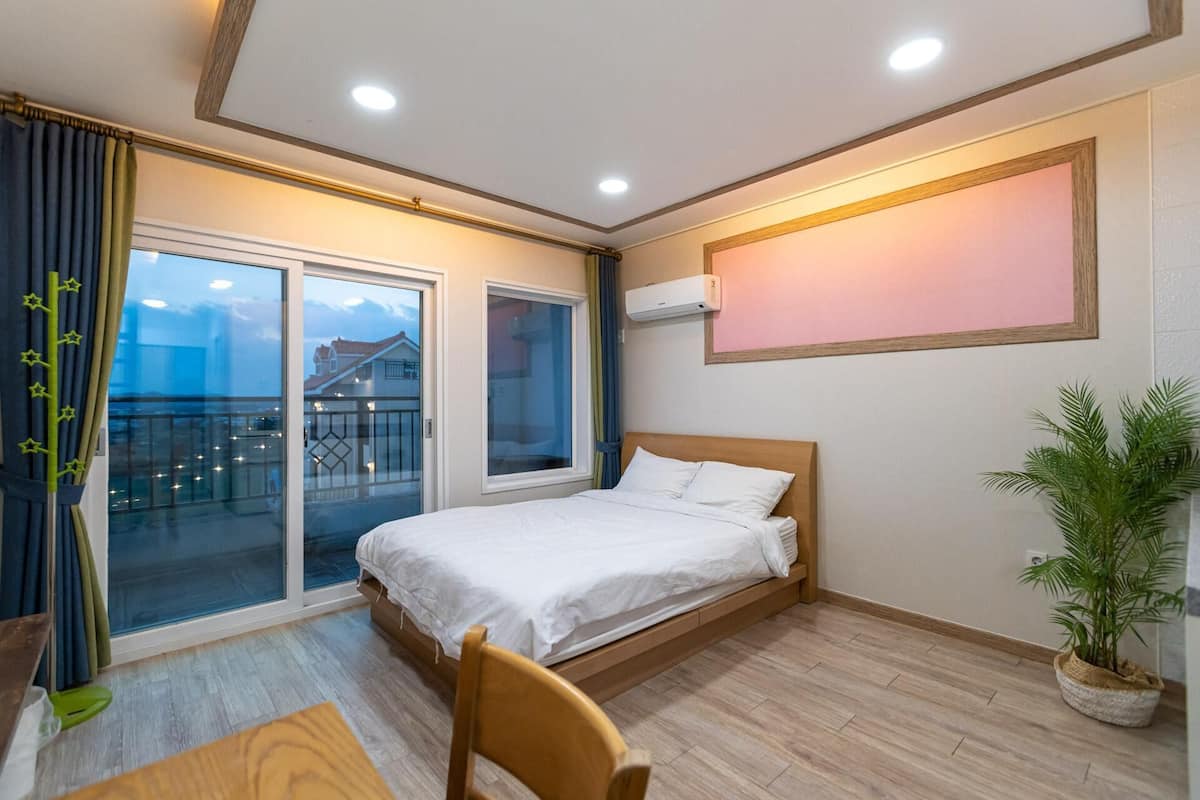 A hotel room with a bed, a chair, a table, a balcony with a view, and an air conditioning unit.