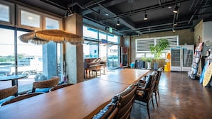 Un vaste espace intérieur comprenant une longue table en bois, plusieurs chaises, un piano et une grande fenêtre donnant sur l’extérieur.