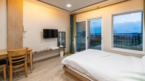 Une chambre avec un lit, un bureau, une chaise, une télévision et un balcon avec vue.