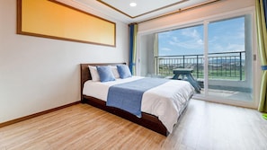 A bedroom with a large bed, a view of the outdoors through a sliding glass door, and a balcony with a table and chairs. - Seogwipo Dobitnarae Resort (Seogwipo)